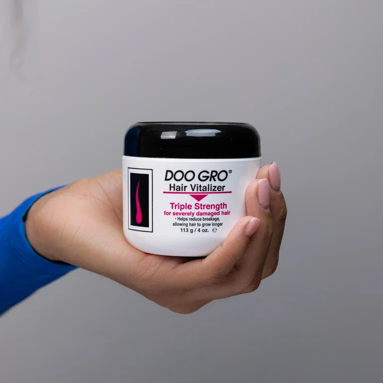 Hand holding a jar of Doo Gro Hair Vitalizer against a gray background