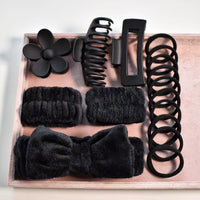 Set of black hair accessories including clips, flowers, and bands on a wooden tray.