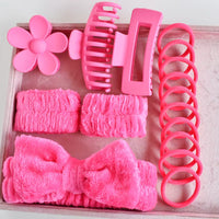 Set of pink hair accessories including a bow, clips, and rubber bands on a wooden tray.